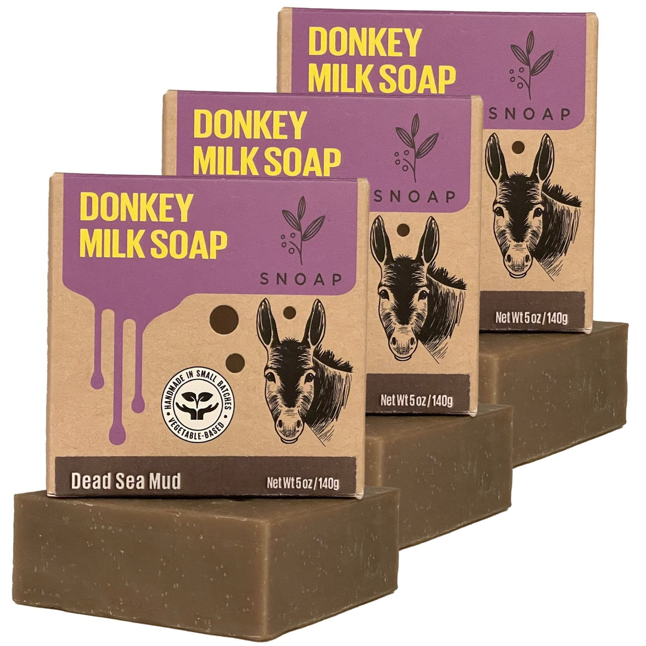 Three bars of dead sea mud donkey milk soap with a dark brown color are stacked in a staggered formation, each below its cardboard box packaging. The boxes are decorated with a sketch of a donkey and the text 'Donkey Milk Soap' and 'SNOAP'.