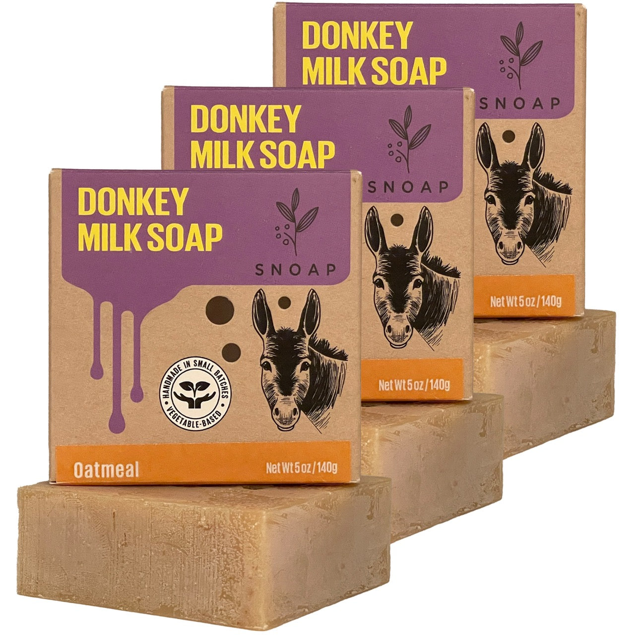 Three bars of oatmeal donkey milk soap with a light brown color are stacked in a staggered formation, each below its cardboard box packaging. The boxes are decorated with a sketch of a donkey and the text 'Donkey Milk Soap' and 'SNOAP'.